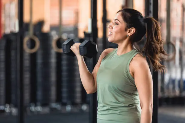 A profile view of a powerful mid adult woman using weights as part of her workout at the fitness center.