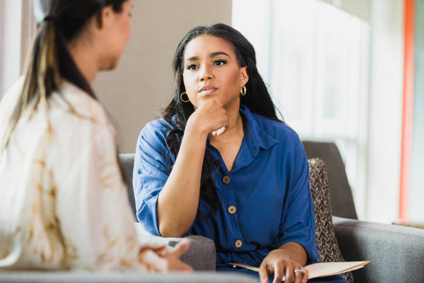 Empathetic therapist listens to female client An empathetic mid adult female counselor sits with her hand on her chin as she listens to the unrecognizable mid adult female client. counseling stock pictures, royalty-free photos & images
