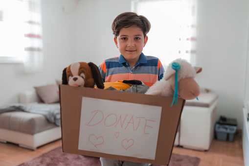 Satisfied young boy holding toy box in his hands labeled as donation box