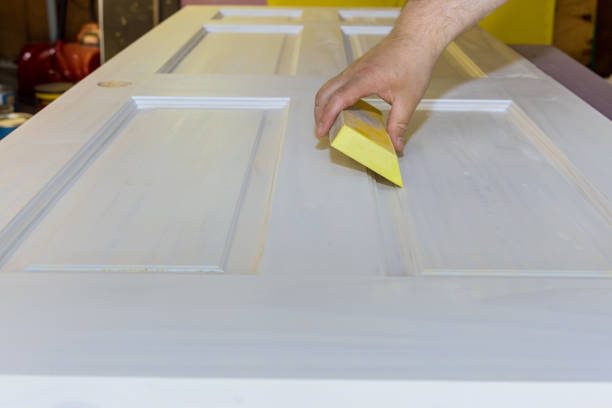 istock Carpenter in work on worker sanding wooden interior door after primer with sanding block 1320396950