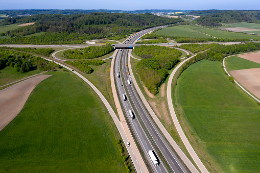 Rural highway and cloverleaf interchange with truck traffic in spring landscape viewed from above.