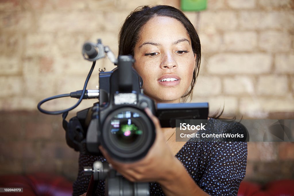 media: camera operator A look of content concentration on the face of a pretty camera operator pleased with the results of her shoot. Camera Operator Stock Photo