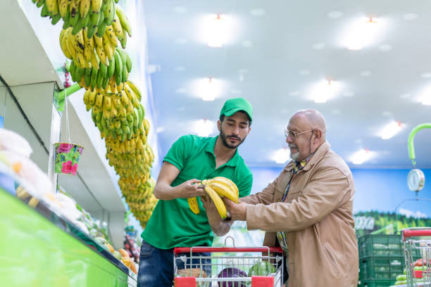 Average age 30-year-old Latino man a grocery store clerk attends to an elderly store customer who asks for help in choosing the best foods,
