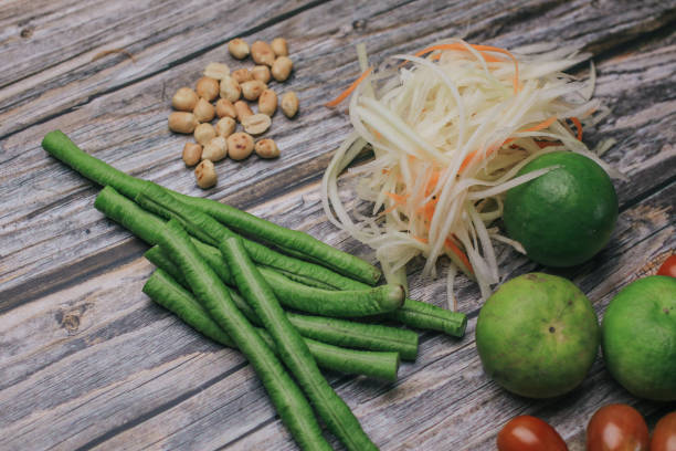 papaya salat (som tam) zutaten auf holztisch hintergrund. das berühmte lokale thailändische streetfood-gericht mit dem geschmack von heiß und würzig. - sour taste green traditional culture lemon stock-fotos und bilder