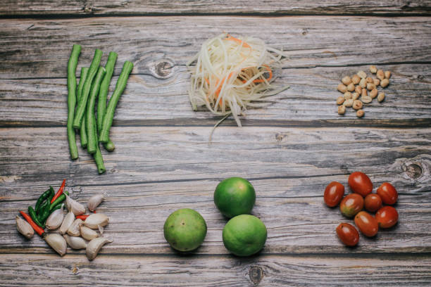 papaya salat (som tam) zutaten auf holztisch hintergrund. das berühmte lokale thailändische streetfood-gericht mit dem geschmack von heiß und würzig. - sour taste green traditional culture lemon stock-fotos und bilder