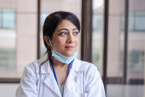 Portrait of a female doctor of Indian descent Portrait of a female doctor of Indian descent wearing a white medical jacket. Staring out the window. Modern hospital setting. self sacrifice stock pictures, royalty-free photos & images