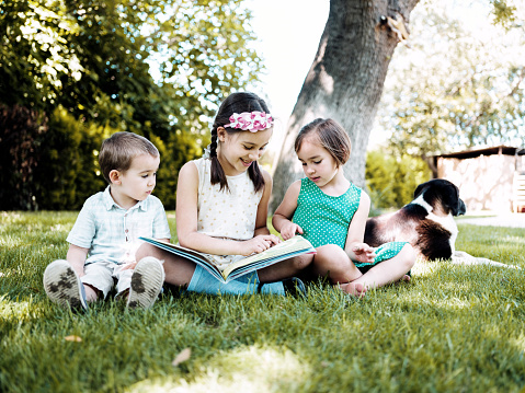Children Reading Book Outdoors In Nature In Summer Season