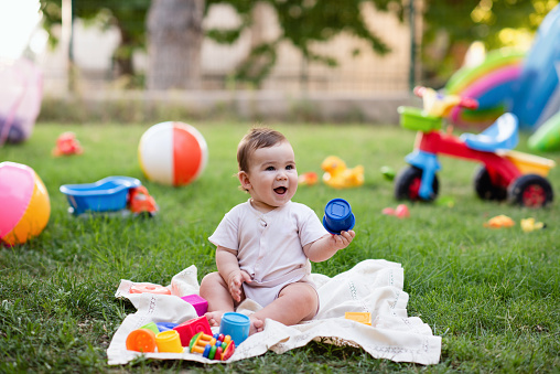 Portrait of Happy Smiling Baby Boy Playing with Toys in Backyard Garden in Summer Season at Sunset