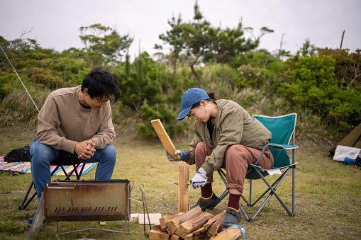 Japanese families camping together. Setting up tents on large green field and eating barbecue for lunch and dinner. Communicating with family and friends.