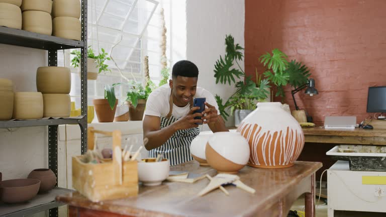 4k video footage of a young man taking pictures of his finished products with a smartphone in a pottery studio