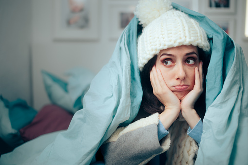 Mujer infeliz sintiéndose fría usando ropa de invierno caliente en el interior photo