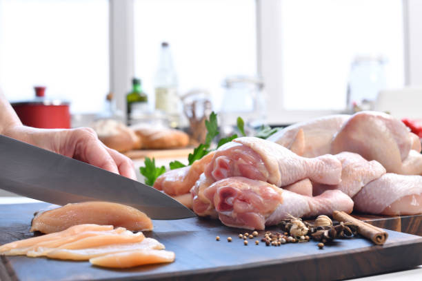 istock Hand slicing fresh raw chicken on a cutting board in the kitchen 1320441959