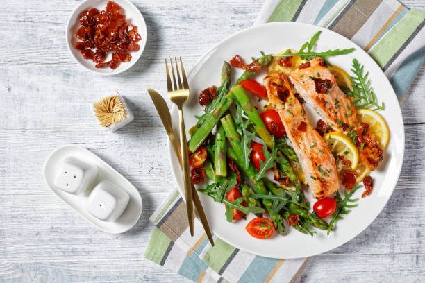 istock grilled salmon fillets with lemon and caramelized bacon served with asparagus, cherry tomatoes, wild rocket salad on a white plate with golden cutlery, flat lay 1320445890