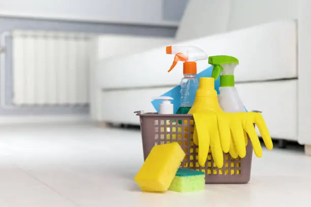 Photo of Cleaning service. Bucket with sponges, chemicals bottles on the background of the room.