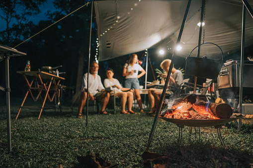 asian chinese family camping dinner with cauldron above campfire firewood boiling with smoke and heat