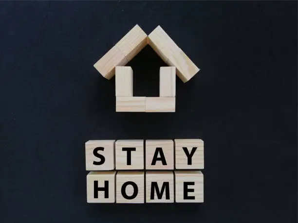 Photo of Stay home wording on wood block concept with black background.