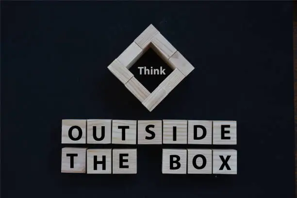 Photo of Think outside the box wording on wood block concept with black background.