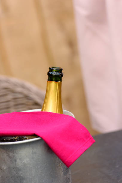 winecooler with champagne bottle Iron winecooler without cork with a magenta serviette waiting for the guests to arrive against lightbrown wooden background anniversaire stock pictures, royalty-free photos & images
