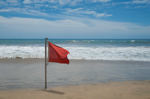 Red flag on an empty beach meaning swimming not allowed due to large waves and rough conditions