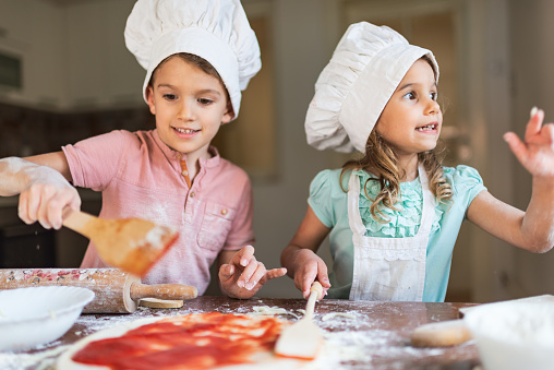 Toddler boy and girl are preparing food in kitchen.