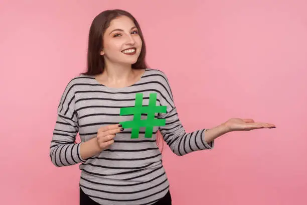 Photo of Follow trends, viral internet topic. Portrait of happy young woman in sweatshirt showing hashtag symbol