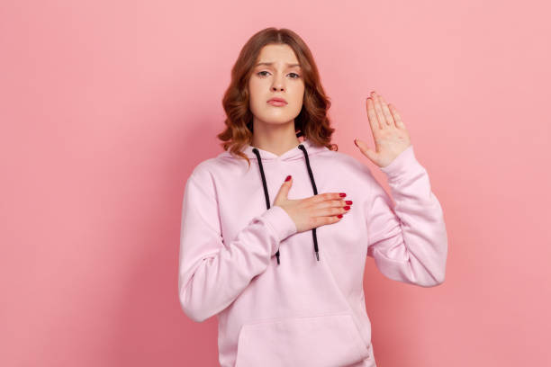 portrait of sincere honest teen girl in hoodie holding hand up and on chest, pledging allegiance, taking oath with responsible expression - proof of love imagens e fotografias de stock