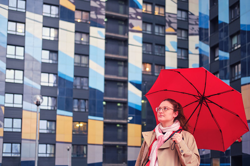 Portrait of a woman with a red umbrella on the background of a multi-colored building in the rain