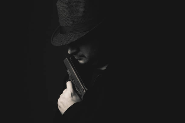 istock Retro man in coat and hat holding a gun 1320469102