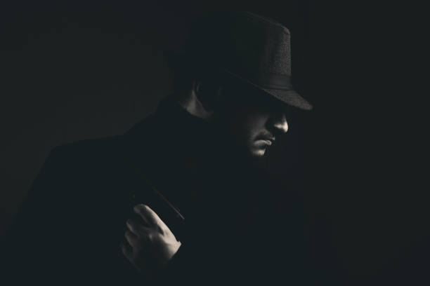 Retro man in coat and hat holding a gun, black and white. Noir style.