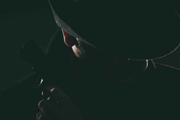 istock Retro man in coat and hat holding a gun 1320469182
