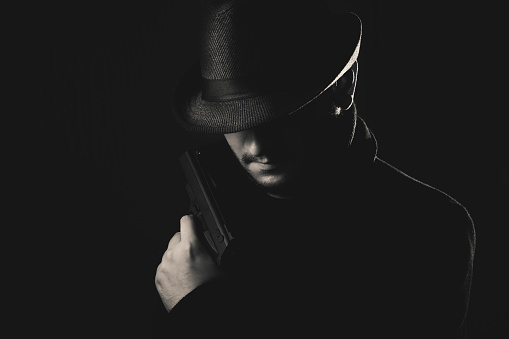 Retro man in coat and hat holding a gun, black and white. Noir style.