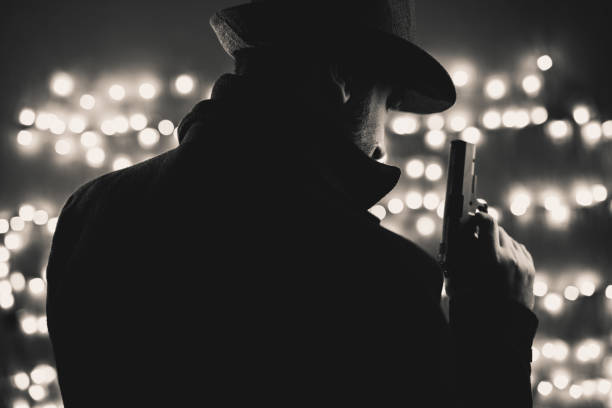 istock Retro man in coat and hat holding a gun 1320469231