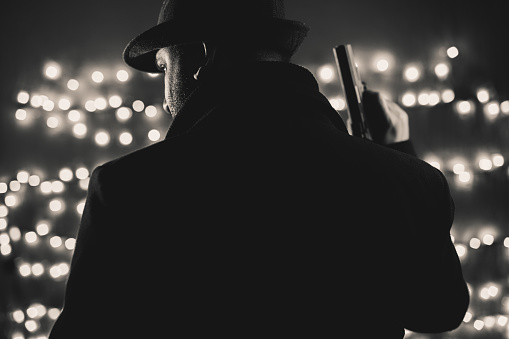 Retro man in coat and hat holding a gun, black and white. Noir style.