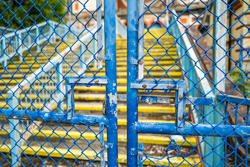 Padlocked blue metal gates with staircase defocused beyond.