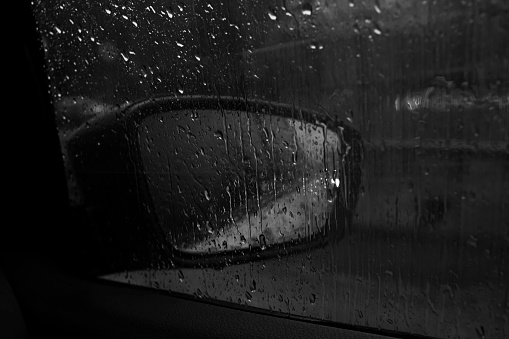 Car side mirror with headlight reflection in rain, black and white