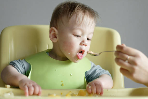 istock little child eats on gray background, mom feeds the baby with a spoon 1320479701