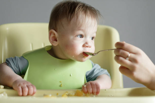 istock little child eats on gray background, mom feeds the baby with a spoon 1320479725