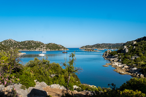 Mediterranean bay, Mediterranean vegetation dominates on the hills, blue sea around 3-4 sailboats\n  boat