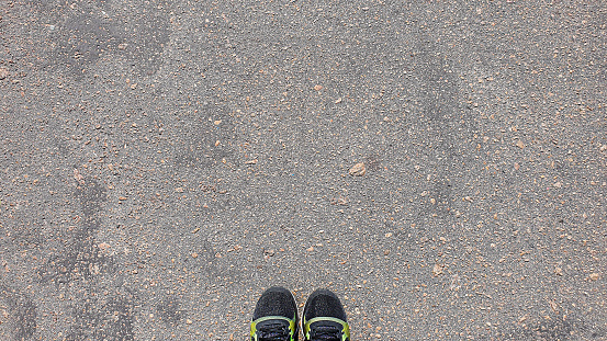 Cracked concrete floor, natural texture. Cement road. Legs on the floor in kratovki. Walking sport concept.
