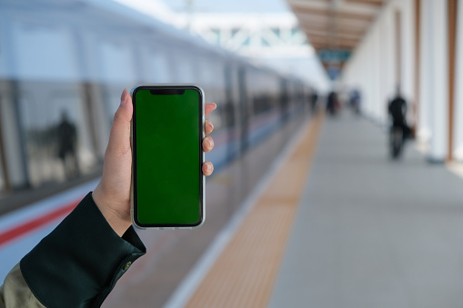 close up hand showing green screen mobile phone on train railway station platform