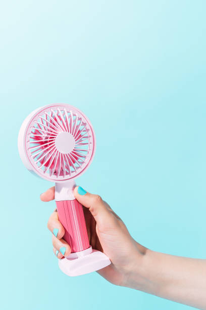 istock unknown person holding an electric fan with blue background. vertical image 1320483602