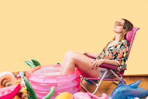 mujer desconocida con ropa de verano sentada en una silla rosa con los pies en una caca infantil, con muchos inflables en el suelo a su alrededor. fiesta en la piscina photo