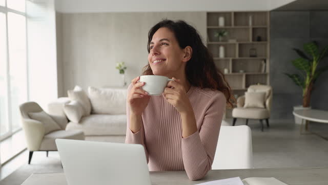 Peaceful woman drinking coffee while sit at desk