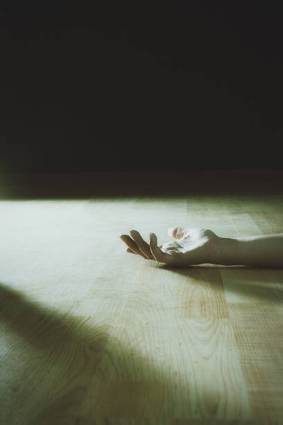Limp hand of a woman lies on a wooden floor, harshly lit from the side: murder victim or sudden illness Woman's hand starkly lit lies on a wooden floor. woman alone dark shadow stock pictures, royalty-free photos & images