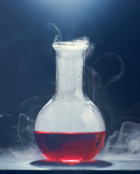 istock Glass flask with a red liquid smokes on a gray background. 1320488530