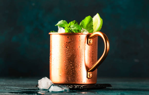 istock Moscow mule alcoholic cocktail in copper mug with lime, ginger beer, vodka and mint. Blue table, copper bar tools 1320490004