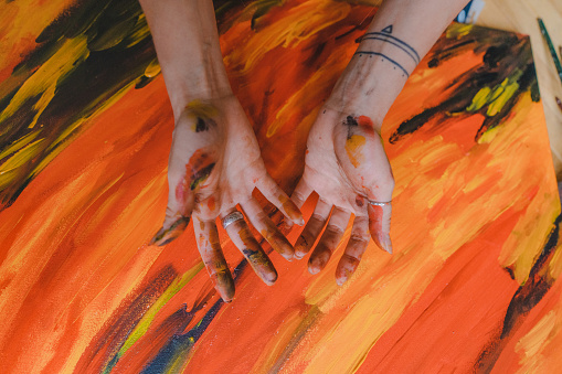 A painter with very delicate hands is mixing paint on her colour palette and painting it onto a large portrait having lost of fun doing that. Portrait