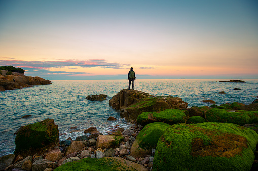 Young man standing on rock looking at sea sunrise