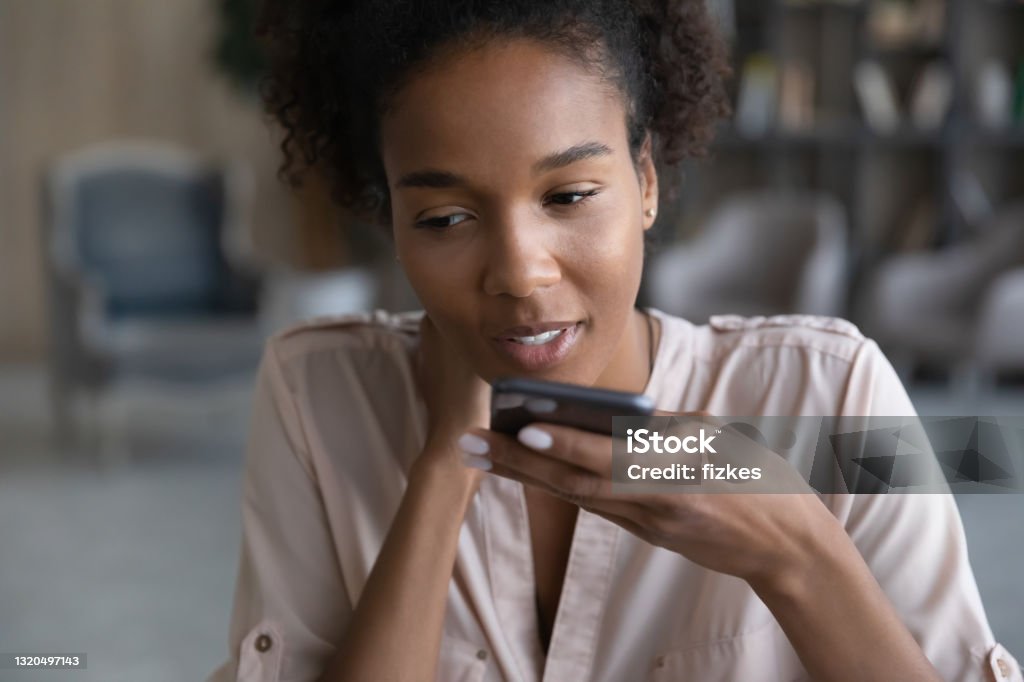 Young african woman dictating audio message on cellphone. Focused young attractive brazilian african american woman recording audio message on smartphone, sending voicemail or holding loudspeaker conversation, dictating information, using virtual assistant. Telephone Stock Photo