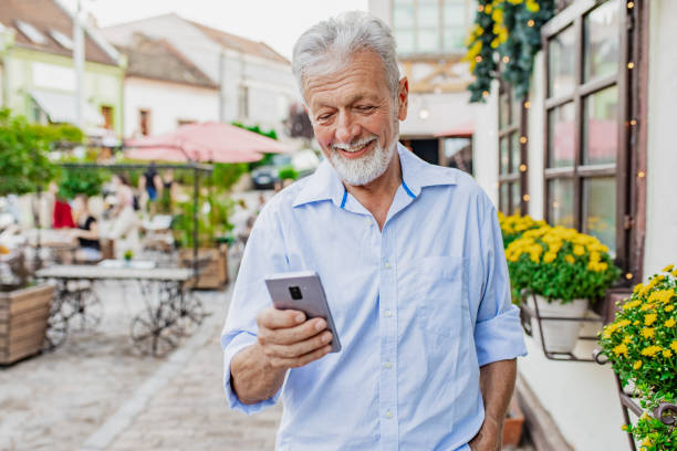istock Happy senior man is using mobile phone on the street 1320497983